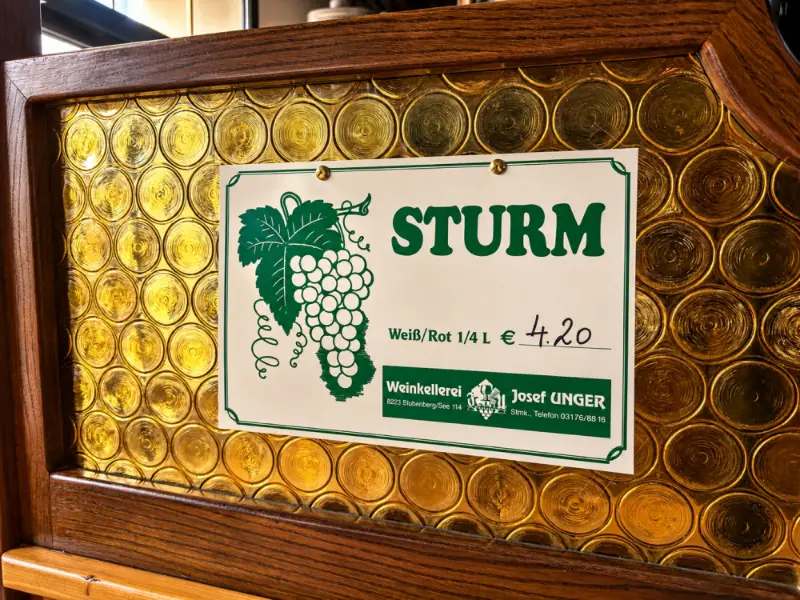 Schild „Sturm, weiß oder rot, ¼ Liter € 4,20“ der Weinkellerei Josef Unger vor einer Butzenscheibe